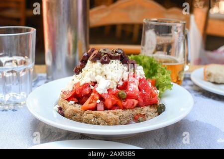 Ein traditioneller griechischer Salat mit gesundem Gemüse, einschließlich Tomaten, Oliven und Salat, mit Fetakäse, serviert in einem Café im Freien. Stockfoto