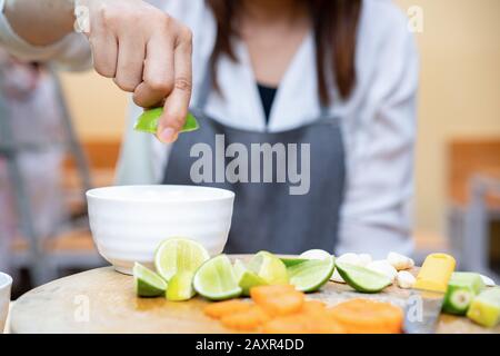 Asian Thai Leute halten und drücken grüne Limette (Zitrone) auf der Oberseite der weißen kleinen Schüssel mit Quater-Limetten auf Holzplatte. Die Umgebung ist einfach Stockfoto