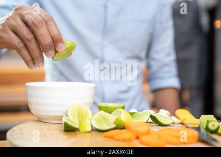 Asian Thai Leute halten und drücken grüne Limette (Zitrone) auf der Oberseite der weißen kleinen Schüssel mit Quater-Limetten auf Holzplatte. Die Umgebung ist einfach Stockfoto