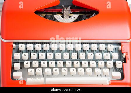 Ein Studio mit einer tragbaren manuellen Schreibmaschine im Retro-Stil mit elfenbeinfarbener Kunststoff-Tastatur und rot-orangefarbenem Metallgehäuse. Stockfoto