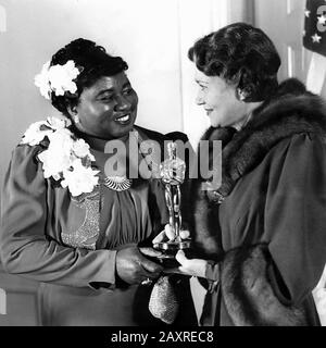 1940, USA: HATTIE McDaniel (* 1892; † 1952) erhält von der Schauspielerin FAY Bainter (* 1893; † 1968) den Oscarpreis, bei der 12. Oscarverleihung 1939 für ihre Rolle der MAMMIE im Film "MIT DEM WIND" ( Über Col Vento , 1939 ) Von Victor Fleming aus dem Roman von Margaret Mitchell . Pubblicity Stills. - FILM - KINO - Porträt - Ritratto - FILM - Premio - Premiazione - Staatuetta - Statuette - Lächeln - sorriso -- Archivio GBB Stockfoto