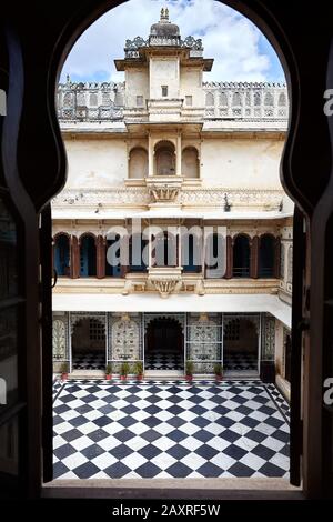 Stadtpalastmuseum mit Schachbrettboden und schöner Architektur in Udaipur, Rajasthan, Indien. Blick von der Silhouette des Bogenfensters. Stockfoto