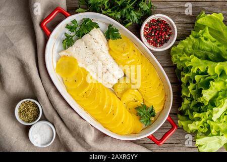 Fisch-Kabeljau im Ofen mit Kartoffeln und Gewürzen gebacken - gesunde Ernährung. Dunkelbrauner Holzhintergrund, Draufsicht. Stockfoto