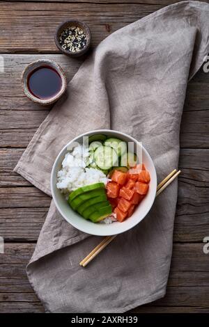 Lachs-Poke-Schüssel mit frischem Fisch, Reis, Gurke, Avocado mit schwarzem und weißem Sesam. Lebensmittelkonzept, Draufsicht, vertikal Stockfoto