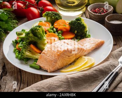 Dampflachs und Gemüse, Paleo, Keto, Fodmap-Ernährung. Weiße Platte auf altem rustikalen Holztisch, Seitenansicht Stockfoto