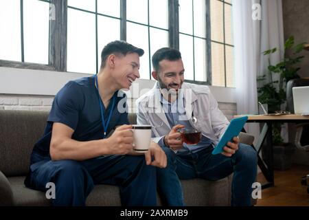 Zwei junge Ärzte haben Tee und lesen etwas auf einer Tablette Stockfoto