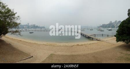 Blick über den Strand und buschfeuerige Rauchschwaden, die über vermoorten Booten hängen, Redleaf Beach und Murray Rose Pool am Sydney Harbour Stockfoto