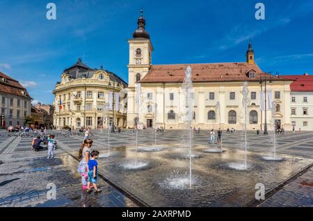 Kinder am Brunnen vor der Römisch-katholischen Kathedrale, Banca Agricola am Piata Stute (großer Platz) in Sibiu, Siebenbürgen, Rumänien Stockfoto