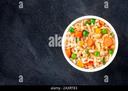 Ramen Schale, instant Soba-nudeln in einem Plastikbecher, mit grünen Erbsen und Karotten, Overhead shot mit Kopie Speicherplatz auf einem schwarzen Hintergrund Stockfoto