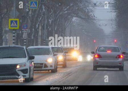 Autos fahren während eines Schneefalls auf einem verschneiten Straße in der Stadt am Abend. Soft Focus Stockfoto