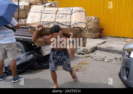 Ein philippinischer Mann führt eine schwere Güterlast in einem Marktgebiet von Cebu City, Philippinen Stockfoto