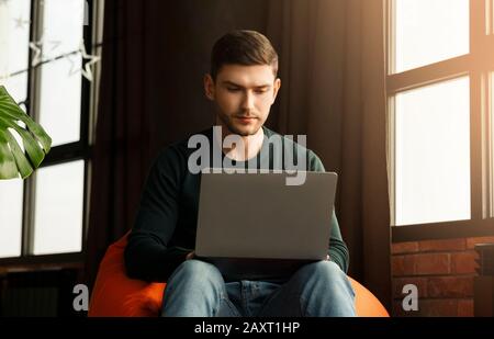 Viel Beschäftigte Freelancer, Die Zu Hause Am Laptop Im Beanbag Chair Arbeiten Stockfoto