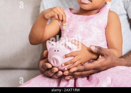 Klein gehäckelte kleine Mädchen, die Münzen in die Schweinebank legen Stockfoto