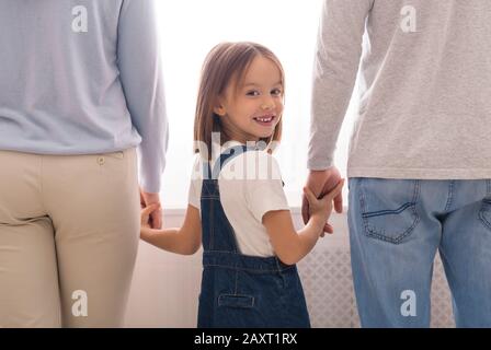 Kleines Mädchen Hält Hände Mit Unerkennbarem Mann Und Frau Und Lächelt Stockfoto