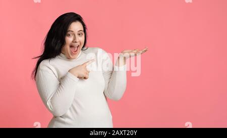 Überfreute plump-Frau, die mit dem Finger auf die offene Handfläche zeigt und etwas zeigt Stockfoto