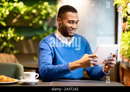 Schwarzer Kerl sitzt im Café und arbeitet an seinem Tablet Stockfoto