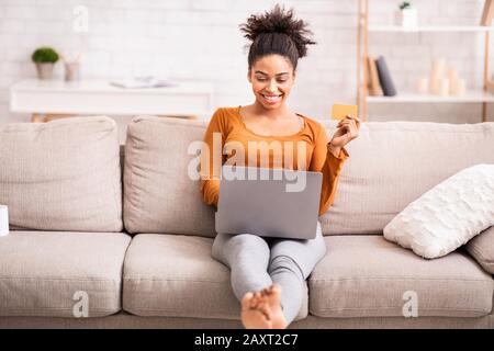 Afro-Frau Mit Laptop Und Kreditkarte Auf Sofa Sitzen Stockfoto