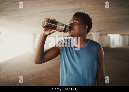 afroamerikanischer junger Mann trinkt nach dem Joggen im Freien Wasser aus der Flasche Stockfoto