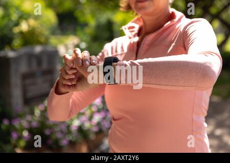 Vorderansicht Mittelteil der Frau im mittleren Alter, die im Park mit Smartwatch arbeitet und sich auf das Workout vorbereitet Stockfoto