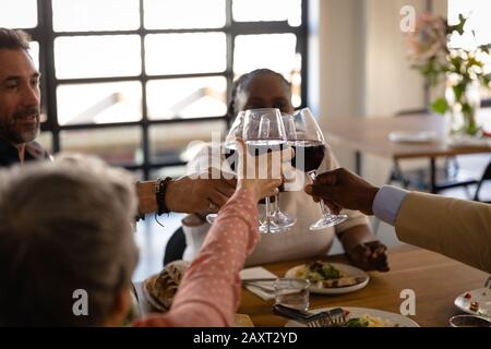 Seitenansicht der älteren multiethnischen Gruppe in der Kochklasse, an einem Tisch sitzen, sich entspannen, eine Brille Rotwein halten und einen Toast machen. Aktiv Stockfoto