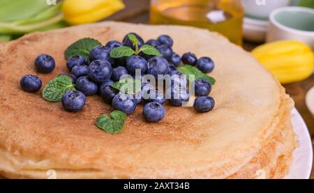 Pfannkuchen mit Blaubeeren und Honig auf einem Teller, auf Holzdach. Traditionelles Gebäck für das russische Festival von Maslenitsa, Freiraum für Text. Nahaufnahme Stockfoto