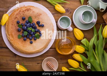 Große traditionelle russische Pfannkuchen mit Beeren und Honig auf einem Holztisch. Backen für den Frühlingsurlaub Shrovetide und einen Blumenstrauß gelber Tulpen. Kopierbereich. Stockfoto