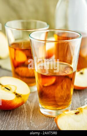 Apfelsaft in Brille. Im Hintergrund gibt es Apfelscheiben und eine Flasche Saft. Stockfoto