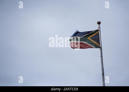 Verwelkte und auf dem Kopf stehende Flagge Südafrikas auf Fahnenmast Stockfoto