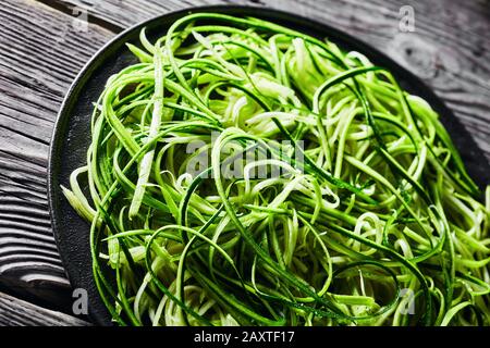 Nahaufnahme frischer Zucchini-Nudeln, Zoodles auf schwarzem Teller auf rustikalem Holztisch, horizontaler Blick von oben Stockfoto