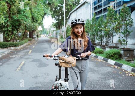 Schöne junge Frauen gehen auf falträder auf der Straße mit Helm und Tragetaschen zu arbeiten Stockfoto