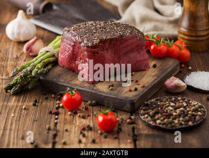 Ein Stück rohes Rindfleisch Oberschale mit Salz und Pfeffer auf Holz Schneidbrett mit Tomaten, Knoblauch und Spargelspitzen auf Holz Küche Tisch. Stockfoto