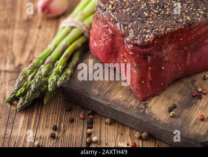 Ein Stück rohes Rindfleisch Oberschale mit Salz und Pfeffer auf Holz Schneidebrett mit Knoblauch und Spargelspitzen auf Holz Küche Tisch. Stockfoto