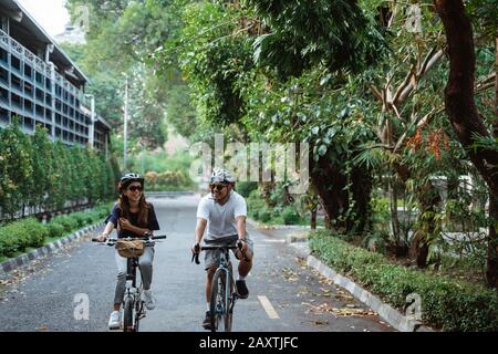 Junge asiatische Paare, die Helme tragen, genießen auf Reisen im Park das gemeinsame Fahrradfahren Stockfoto