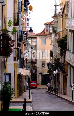 Enge Gasse in Lissabon. Hellblauer Himmel mit stuckierten Fertighäusern und trocknenden Tüchern, die an Trocknern hängen. Balkone und Wände in Pastellfarbe Stockfoto