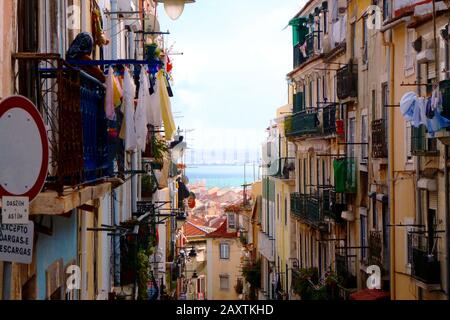 Enge Gasse in Lissabon. Hellblauer Himmel mit stuckierten Fertighäusern und trocknenden Tüchern, die an Trocknern hängen. Balkone und Wände in Pastellfarbe Stockfoto