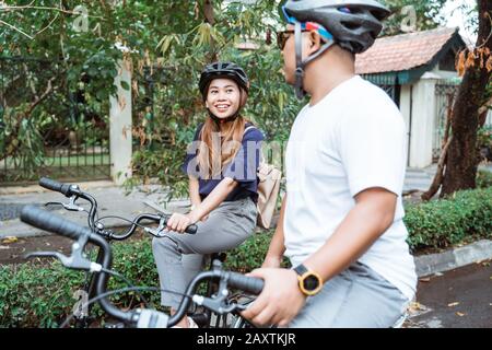Junge asiatische Paare, die Helme tragen, genießen auf Reisen im Park das gemeinsame Fahrradfahren Stockfoto