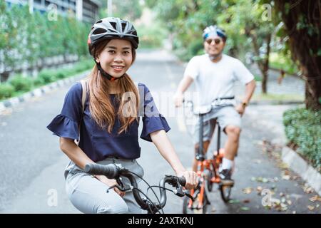Junge asiatische Paare, die Helme tragen, genießen auf Reisen im Park das gemeinsame Fahrradfahren