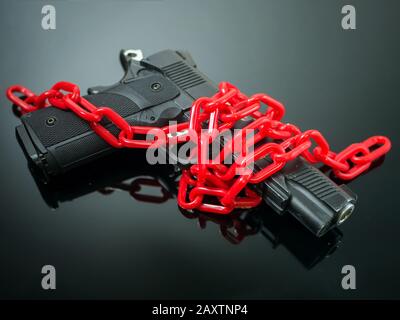 Reformgewehr-Steuerungskonzept: Rote Kette um Handfeuerwaffe auf schwarzem Spiegel mit Spotlight glänzt bis zur Waffe Stockfoto