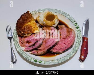 Ein köstliches traditionelles Abendessen mit Sonntagsbraten - Scheiben von mittelseltenem Roastbeef und Soße, Kartoffelpüree und Yorkshire Pudding auf einem Porzellanboden Stockfoto