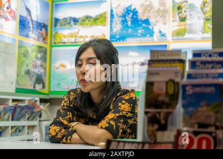 Thailand, Phuket, Patong, 1. Februar 2020: Süße Thailänderin, Verkäuferin von Touristenführungen und Tourpaketen, abends auf der Straße von gelangweilt Stockfoto