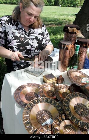 Eine Frau macht mit Kupferplatten und Souvenirs aus Hammer in der Straße von Sofia, Bulgarien, 2012 ( Handwerker schnitzen ein Metallgefäß senkrecht) Stockfoto