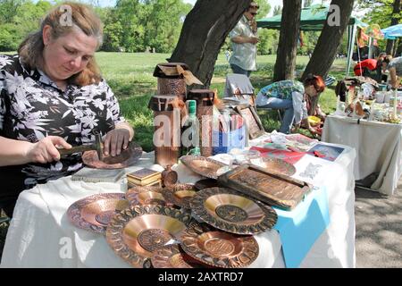 Eine Frau macht mit Kupferplatten und Souvenirs aus Hammer in der Straße von Sofia, Bulgarien, 2012 ( Handwerker schnitzen ein Metallgefäß) Stockfoto