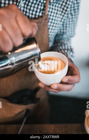 Vertikale Aufnahme eines Mannes, der Milch in einen Cappuccino gießt tasse in einem Café Stockfoto