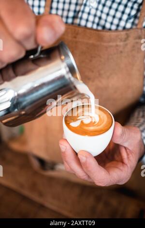 Vertikale Aufnahme eines Mannes, der Milch in einen Cappuccino gießt tasse in einem Café Stockfoto
