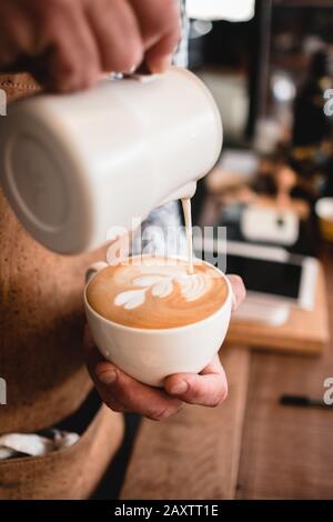 Vertikale Aufnahme eines Mannes, der Milch in einen Cappuccino gießt tasse in einem Café Stockfoto