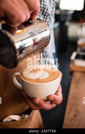 Vertikale Aufnahme eines Mannes, der Milch in einen Cappuccino gießt tasse in einem Café Stockfoto