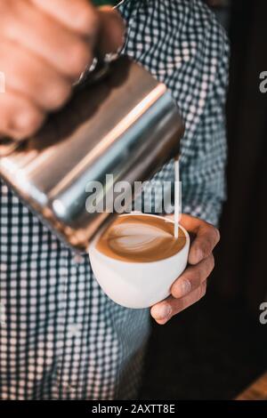 Vertikale Aufnahme eines Mannes, der eine geschäumte Milch hineingießt Eine Tasse Cappuccino Stockfoto