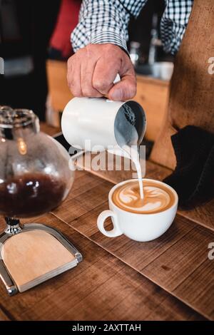 Vertikaler Schuss Mann Gießen Milch in Cappuccino Stockfoto