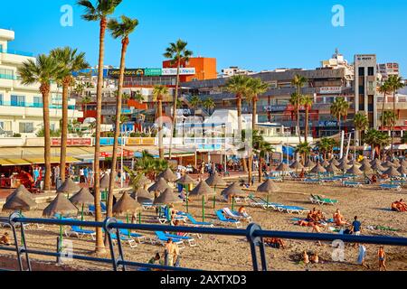 Spanien, Tenera, Adeje - 17. Dezember 2018: Sonnenschirme und Sonnenanbeter bei Sonnenuntergang. Badeort. Stockfoto