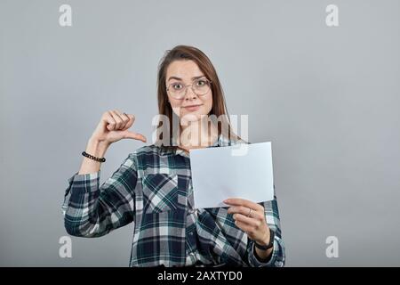 Fröhliche Frau mit Brille hält ein weißes Blatt Papier in der Hand, zeigt sich Stockfoto